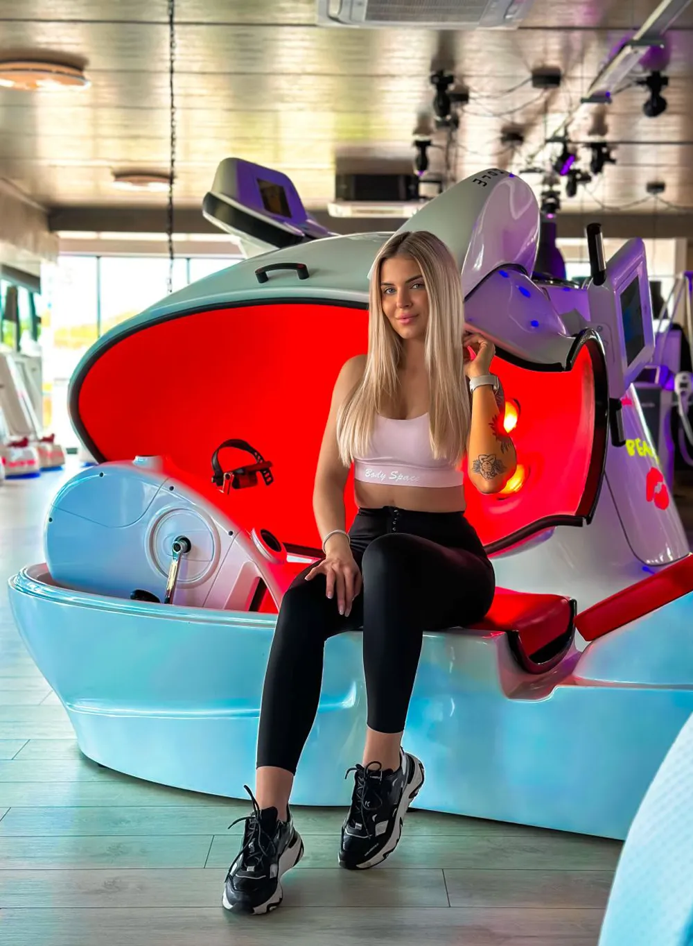 Kobieta korzystająca z urządzenia Body Space™ z czerwonym podświetleniem w nowoczesnym studiu fitness