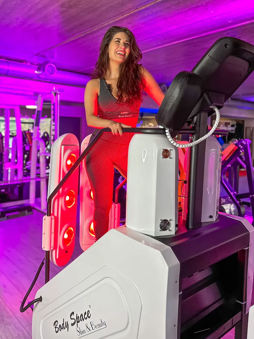 Uśmiechnięta kobieta w czerwonym stroju ćwiczy na InfraRed Stepper Body Space® otoczona światłem IR